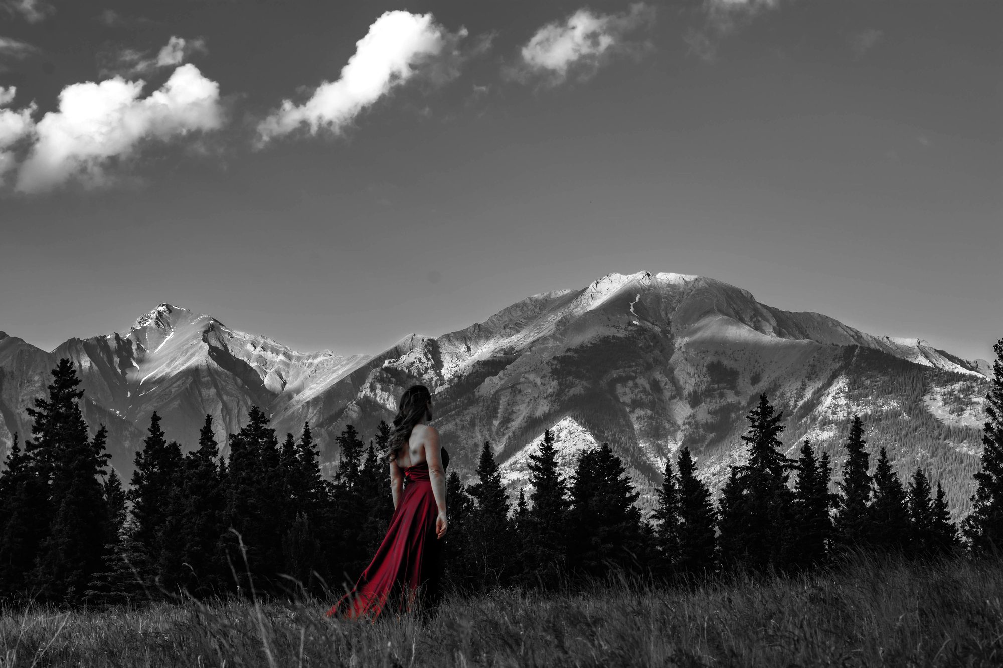 Julia in a red gown in a wide alpine meadow beneath snow-dusted peaks