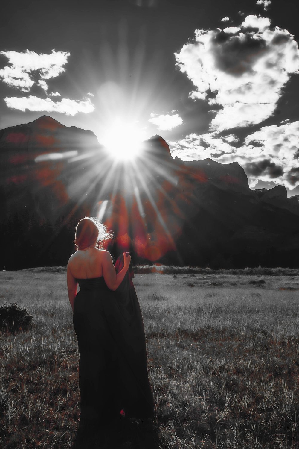 Julia in a red gown facing the mountains at sunset