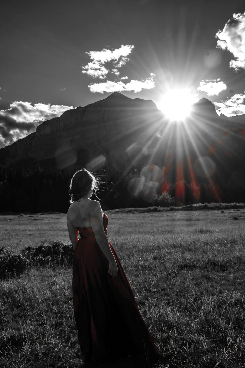 Julia at golden hour in a mountain meadow, the sun bursting over the peak behind her